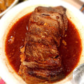 Beef dish in a red sauce on a white plate with Chinese text in the background