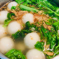 Bowl of soup with white balls, green vegetables, and brown bits. 客家鹹湯圓