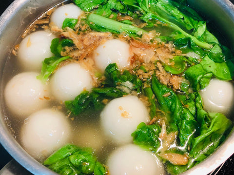 Bowl of soup with white balls, green vegetables, and brown bits. 客家鹹湯圓